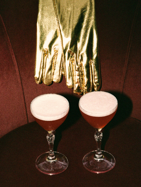 Cocktail en coupe avec garniture grenadine pos&eacute; sur table en bois brut &agrave; c&ocirc;t&eacute; d'une lampe vintage &ndash; bar La Sauvageonne, Ramatuelle