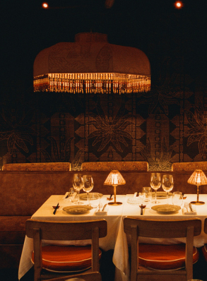 Longue table dress&eacute;e en terrasse couverte la nuit, lampe suspendue &agrave; franges et tabourets en bois brut &ndash; restaurant La Sauvageonne, Ramatuelle